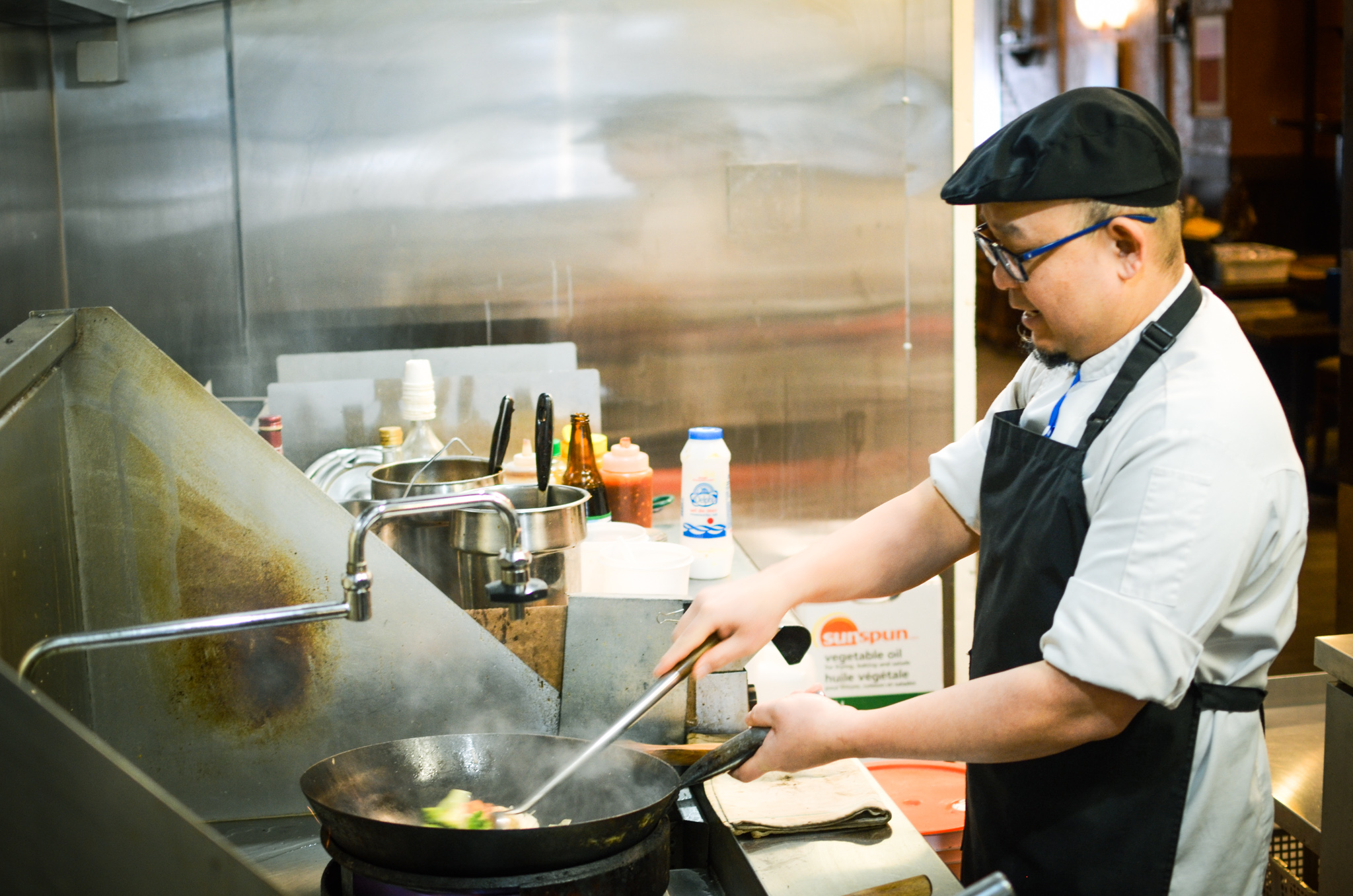 A man cooking food in a wok at a kitchen stove